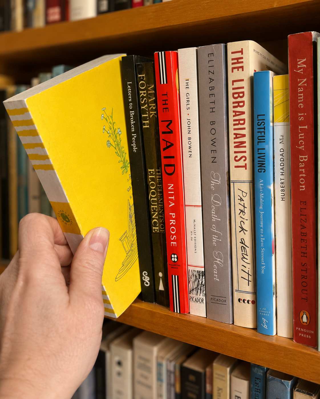 A hand pulling a yellow paperback from a colorful shelf of books
